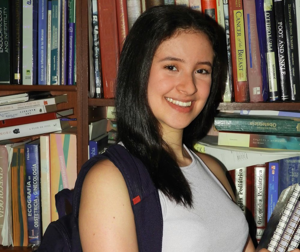 A student with a backpack in a library, smiling.